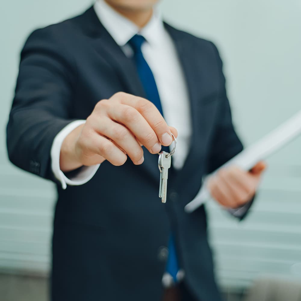 A Man in a suit holds a set of keys to your new home.