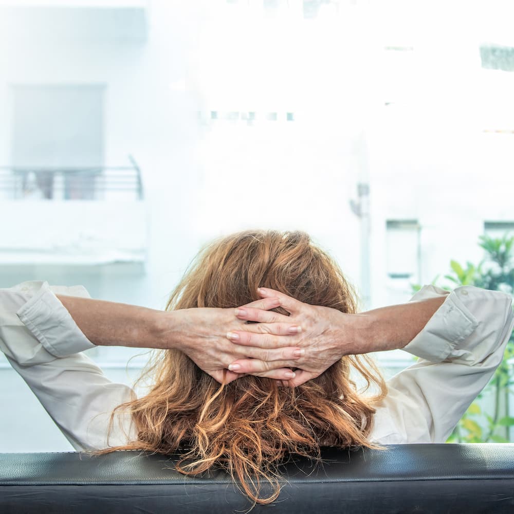 A relaxed woman with red hair faces away from the camera looking out her balcony.